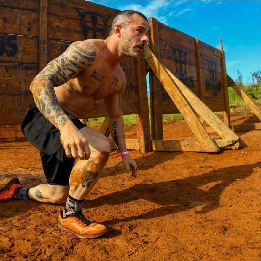 Rafael Sanches ajoelhado em pista de obstáculos de terra vermelha, com tênis laranja